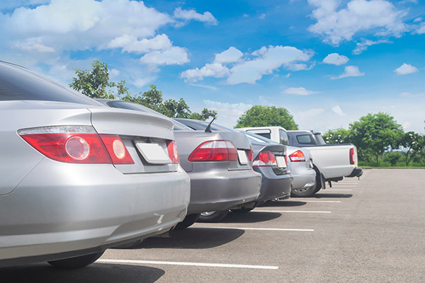 Row of cars in large asphalt parking lot.